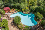 Outdoor swimming pool surrounded by wrought iron security fence and various shrubs and trees in luxury residential backyard, high angle view