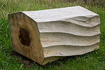 Close up of carved piece of tree trunk with wave pattern lying on grass.