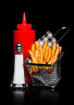 Basket of freshly made southern fries with ketchup and salt black paper on black studio background