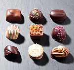 Assortment of luxury white and dark chocolate candies variety on black stone background with hard shadows