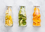 Bottles of fresh summer water with oranges with limes and lemons slices on marble background
