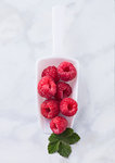 White scoop with fresh raw organic raspberries on marble background