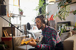 Young male musician recording music, playing guitar at microphone in apartment