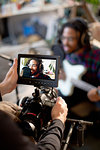 Videographer filming young male musician singing and playing guitar