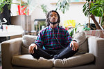 Serene young man meditating with headphones on apartment sofa