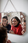 Young women friends getting ready, applying makeup in bathroom mirror