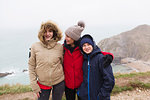 Portrait happy family in warm clothing standing on cliff overlooking ocean