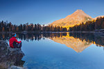 Hiker take a break to admire sunrise on lake Saoseo and Corn da Murasciola mount, Poschiavo, val di Campo, Canton of Graubunden, Switzerland, Europe