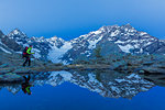 A hiker walks at dusk near a lake that mirrored the mountain range of Mount Disgrazia. Chiareggio valley, Valmalenco, Valtellina, Lombardy, Italy, Europe.