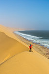 Tourist admiring the ocean from the top of the sand dunes,Sandwich Harbour,Namib Naukluft National Park,Namibia,Africa