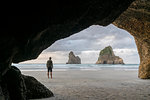 Man staring at two of the Archway Islands. Wharariki beach, Puponga, Tasman district, South Island, New Zealand.