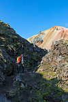 Graenagil footpath: a trekker is walking through the Laugahraun lava field in Landmannalaugar, the Brennisteinsalda mountain on background (Fjallabak Nature Reserve, Highlands, Southern Region, Iceland, Europe) (MR)