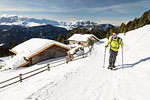 a hiker is walking with snowshoes in Val Gardena with two typical mountain huts in the background, Bolzano province, South Tyrol, Trentino Alto Adige, Italy