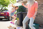 Mother and playful daughter breaking down cardboard for recycling outside house