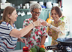 Active senior women friends cooking, toasting cocktails in kitchen