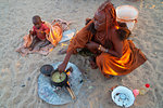 One senior red ochred Himba woman with her child cooking on an open fire, Puros Village, nearr Sesfontein, Namibia, Africa