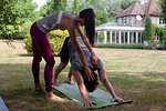 Female yoga teacher teaching young man yoga in garden, downward facing dog pose