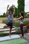 Female yoga teacher teaching young man yoga in garden, tree pose