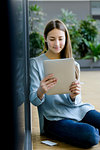 Woman leaning on glass wall using digital tablet