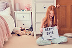 Girl holding up sign on bedroom floor