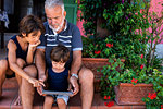 Grandfather sitting with grandsons on front door steps