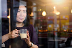 Mid adult woman with coffee looking out from cafe window seat