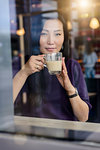 Mid adult woman with coffee looking out from cafe window seat, portrait