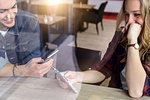 Male and female students looking at smartphone in cafe window seat, view through window