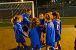 Soccer coach and girls soccer team in huddle on field at night