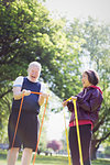 Enthusiastic active senior couple exercising, using resistance bands in sunny park