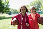 Portrait happy, active senior women friends playing basketball in sunny park