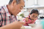 Grandfather and granddaughter eating noodles in kitchen