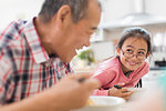 Smiling grandfather and granddaughter eating at table