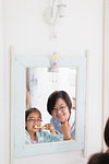 Mother watching daughter brushing teeth in bathroom mirror