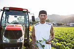 Japanese farmer standing in front of red tractor in a soy bean field, looking at camera.