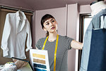 Japanese female fashion designer working in her studio, looking at garment on dressmaker's model.