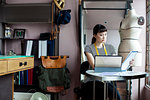 Japanese female fashion designer working in her studio, sitting at table, looking at fabric samples.