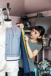 Japanese female fashion designer working on a garment on a dressmaker's model in a studio.