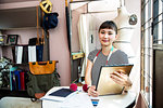 Japanese female fashion designer working in her studio, smiling at camera.