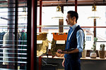 Japanese salesman with moustache wearing glasses standing in clothing store, holding digital tablet.