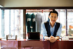 Japanese salesman with moustache wearing glasses standing at counter in clothing store, smiling at camera.