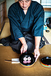 Japanese man wearing traditional kimono knelling on floor, holding a bowl with Wagashi, sweets traditionally served during a Japanese Tea Ceremony.