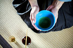 High angle close up of Japanese man wearing traditional kimono kneeling on floor holding blue bowl with Matcha tea during tea ceremony.