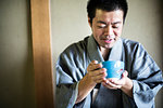 Japanese man wearing traditional kimono holding blue tea bowl during tea ceremony.