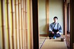 Japanese man wearing traditional kimono kneeling on tatami mat during tea ceremony.