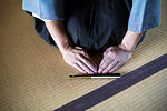 High angle close up of Japanese man kneeling on tatami mat in front of Sensu fan during a tea ceremony, used as a greeting.