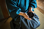 High angle close up of Japanese man wearing kimono holding tea bowl during tea ceremony.