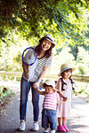 Smiling Japanese woman holding butterfly net and two girls wearing sun hats standing on path, looking at camera.