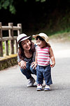 Smiling Japanese woman kneeling next to little girl wearing sun hat, striped top and jeans.