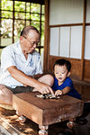 Japanese man and little boy sitting on floor on porch of traditional Japanese house, playing Go.